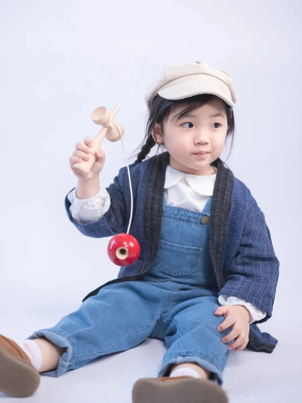 A young girl sitting in denim overalls and a Hand-cranked Kids Kimono jacket in Moon Night blue at Grandmama Store in Hong Kong.