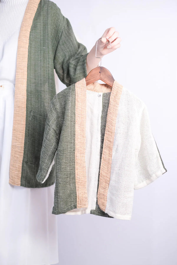 A Hand-cranked Kids Kimono jacket on a wooden hanger in the Yakushima olive green and beige colorway at Grandmama Store in Hong Kong.