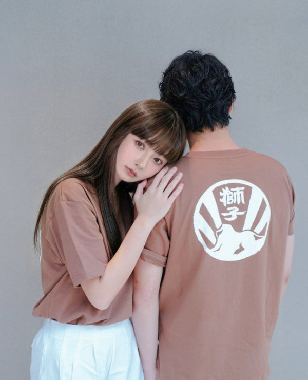 A couple posing together in matching brown Kamon Tee-LionRock t-shirts featuring the white circular lion back crest at Grandmama Store in Hong Kong.