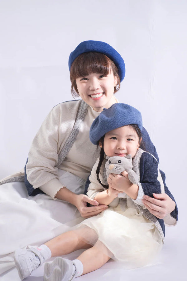 A mother and daughter wearing matching Hand-cranked Kids Kimono cardigan jackets in the Mt. Fuji colorway with blue berets at Grandmama Store in Hong Kong.