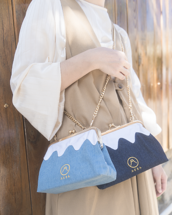 A woman holding both light blue and dark blue Mt. Fuji Pocket Bags with gold chain straps at Grandmama Store in Hong Kong.