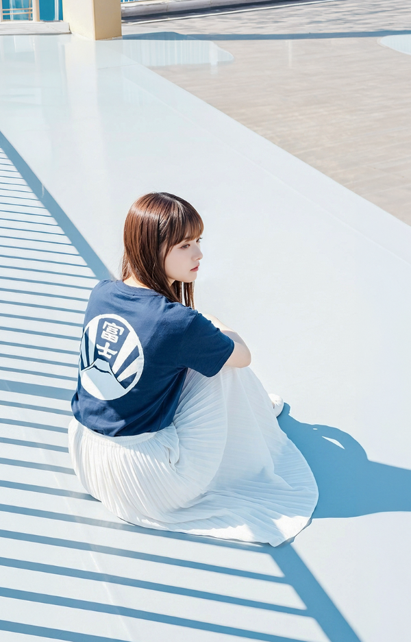 A woman sitting on a sunny rooftop wearing a navy blue Kamon Tee-Fujisan t-shirt with a white circular Mt. Fuji crest print on the back at Grandmama Store in Hong Kong.