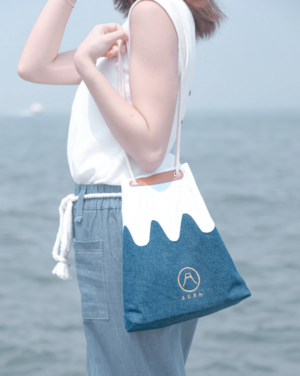A woman wearing a navy blue Mt. Fuji sake bag over her shoulder by the sea at Grandmama Store in Hong Kong.