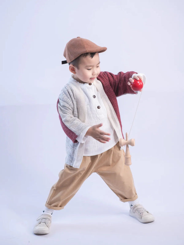 A young boy playing with a kendama wearing a Hand-cranked Kids Kimono jacket in Tokyo Tower red at Grandmama Store in Hong Kong.