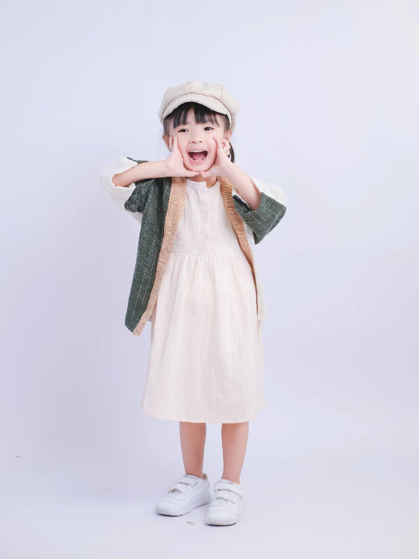 A young girl in a white dress modeling a Hand-cranked Kids Kimono jacket in Yakushima green at Grandmama Store in Hong Kong.