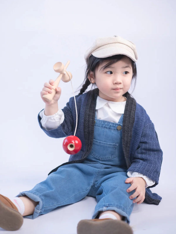 A young girl sitting in denim overalls and a Hand-cranked Kids Kimono jacket in Moon Night blue at Grandmama Store in Hong Kong.