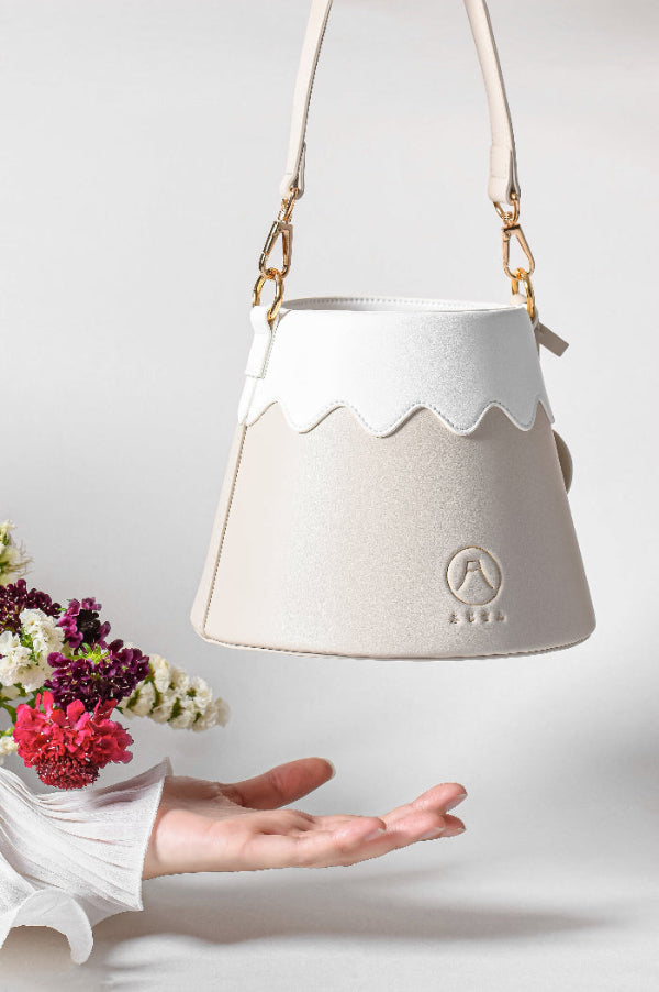 Beige Mt. Fuji Goen Bag with scalloped snow-cap trim suspended over colorful flowers at Grandmama Store in Hong Kong.