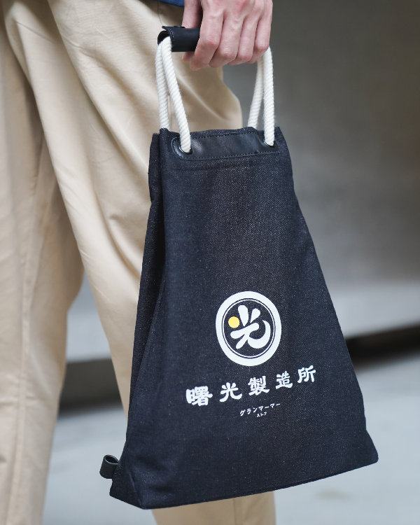 Close-up of a model carrying the Light of Dawn Sake Bag in Black Denim by hand at Grandmama Store in Hong Kong.