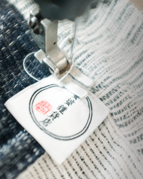 Close-up of a sewing machine stitching the brand label onto a Hand-cranked Kimono at Grandmama Store in Hong Kong.