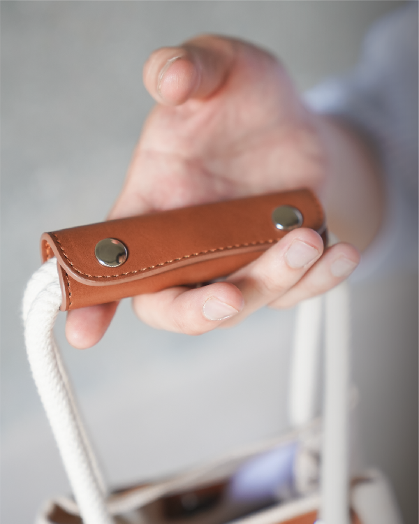 Close-up of hand holding the leather handle wrap of the Light of Dawn Sake Bag in Linen at Grandmama Store in Hong Kong.