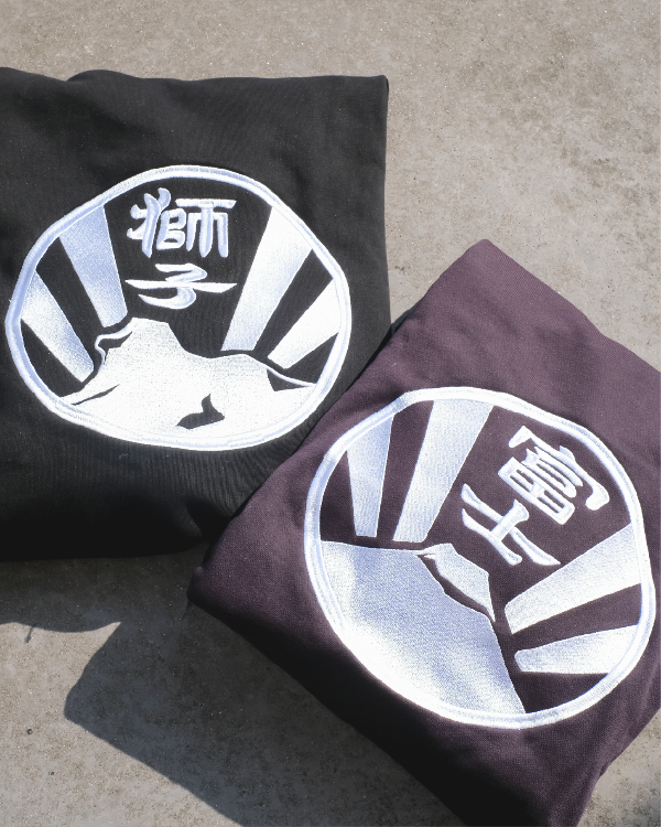 Close-up view of embroidered back crests on folded black and dark purple Kamon Hoodies at Grandmama Store in Hong Kong.