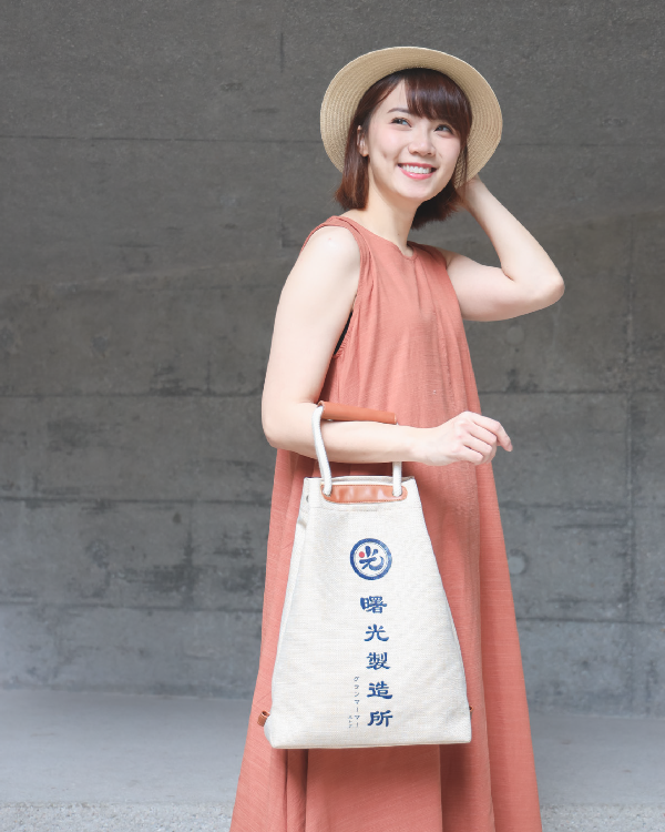 Female model holding the Light of Dawn Sake Bag in Linen by hand at Grandmama Store in Hong Kong.