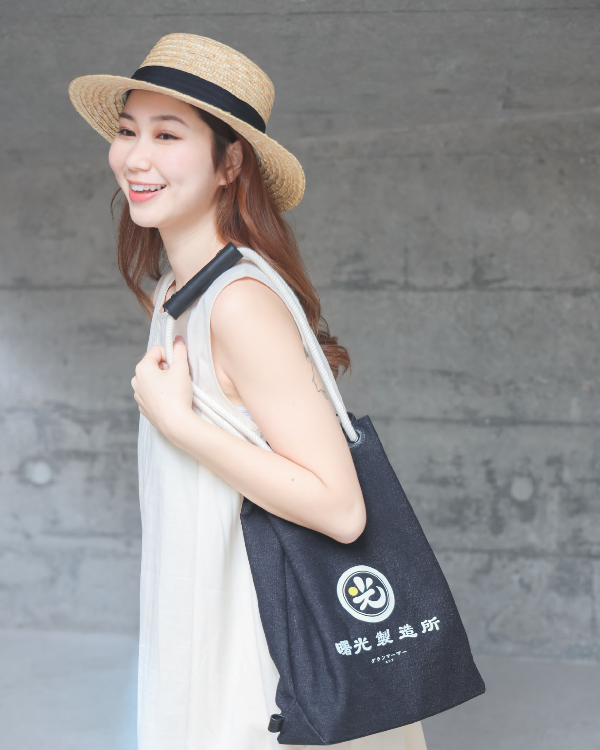 Female model wearing a straw hat carrying the Light of Dawn Sake Bag in Black Denim over her shoulder at Grandmama Store in Hong Kong.