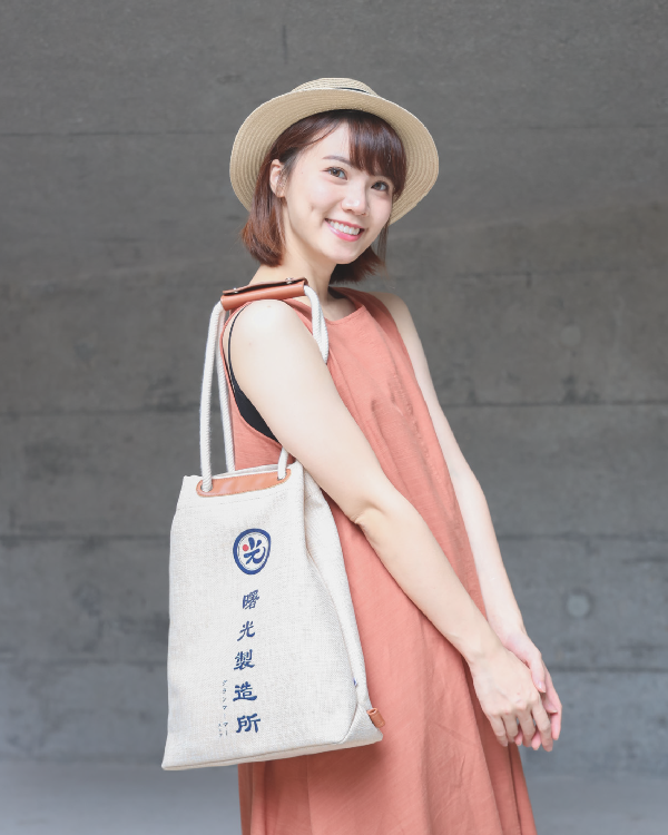 Female model wearing a straw hat carrying the Light of Dawn Sake Bag in Linen over her shoulder at Grandmama Store in Hong Kong.