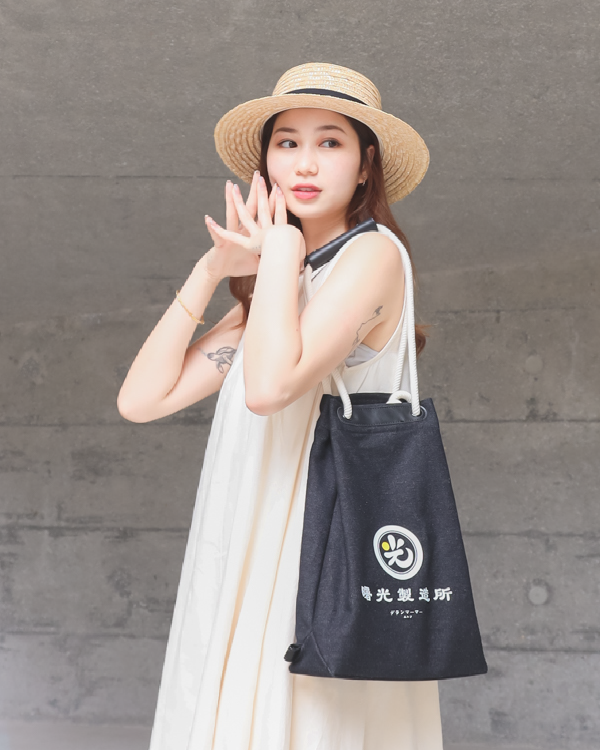 Female model wearing a straw hat posing with the Light of Dawn Sake Bag in Black Denim at Grandmama Store in Hong Kong.