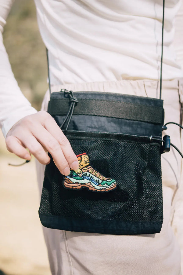 Hand attaching embroidered boot patch to black Yama Multifunctional Bag at Grandmama Store in Hong Kong.
