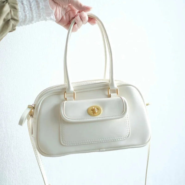 Hand holding an off-white Minimalist Convertible Leather Bag with gold twist-lock closure at Grandmama Store in Hong Kong.