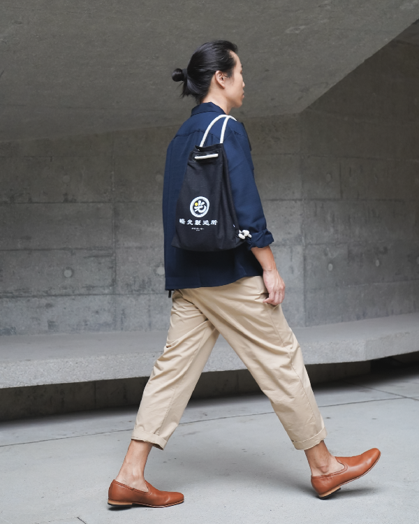 Profile view of a model walking with the Light of Dawn Sake Bag in Black Denim on his shoulder at Grandmama Store in Hong Kong.