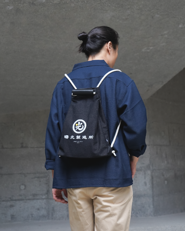 Rear view of a model wearing the Light of Dawn Sake Bag in Black Denim as a backpack at Grandmama Store in Hong Kong.