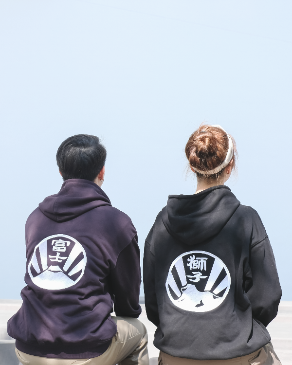 Seated back view of two models wearing dark purple and black Kamon Hoodies outdoors at Grandmama Store in Hong Kong.