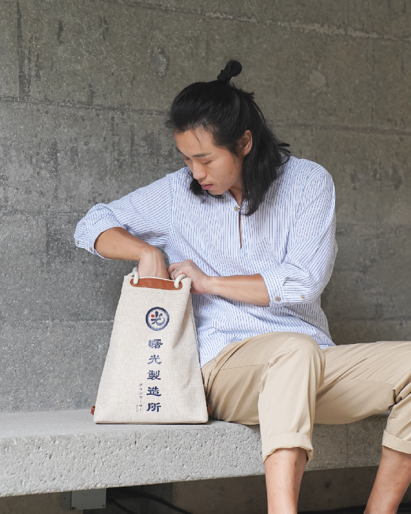 Seated male model accessing the Light of Dawn Sake Bag in Linen at Grandmama Store in Hong Kong.