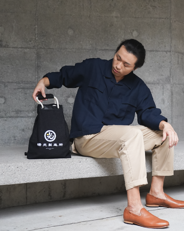 Seated male model holding the Light of Dawn Sake Bag in Black Denim at Grandmama Store in Hong Kong.