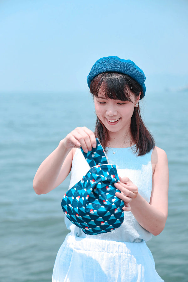 Smiling model holding a blue Fuji Handled Moonshell Bag near the ocean at Grandmama Store in Hong Kong.