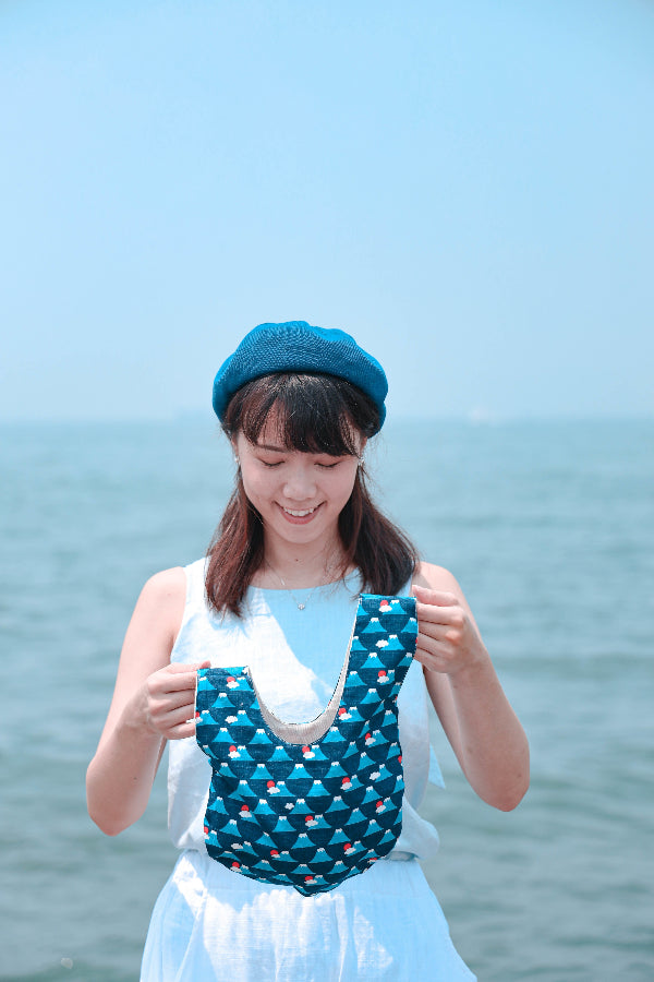 Woman holding a blue Fuji Handled Moonshell Bag outdoors against the sea at Grandmama Store in Hong Kong.