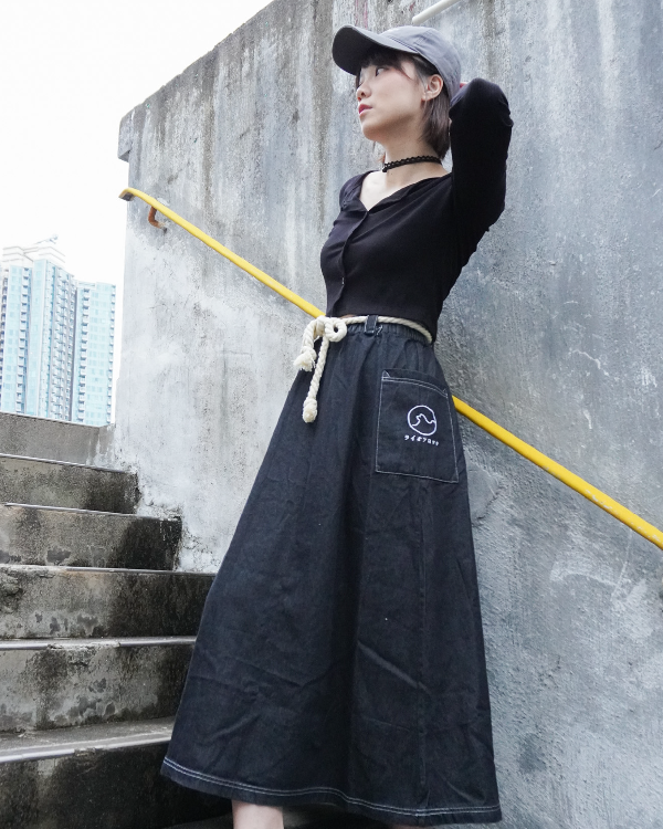 Woman wearing the black Kamon Denim Dress and baseball cap standing on outdoor concrete stairs at Grandmama Store in Hong Kong.