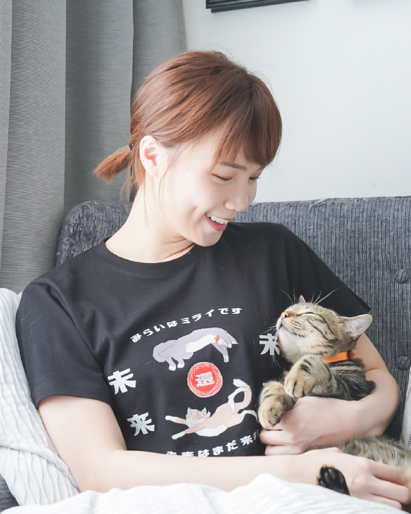 Woman wearing the black Lazy Cat Tee holding a sleeping cat on a sofa at Grandmama Store in Hong Kong.