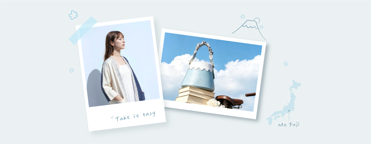 A Polaroid-style photo of a female model with long brown hair wearing a white camisole paired with the Hand-cranked Kimono cardigan from the Fuji Series, with 'Take it easy' written below. The image displays the textured, heavy slub-knit cotton material of the cream cardigan body, featuring indigo blue corduroy trim along the collar, front opening, and cuffs, set against a soft blue background at Grandmama Store in Hong Kong