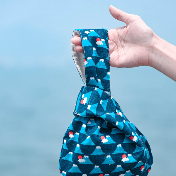 Hand holding a blue Fuji Handled Moonshell Bag outdoors with sea background at Grandmama Store in Hong Kong.